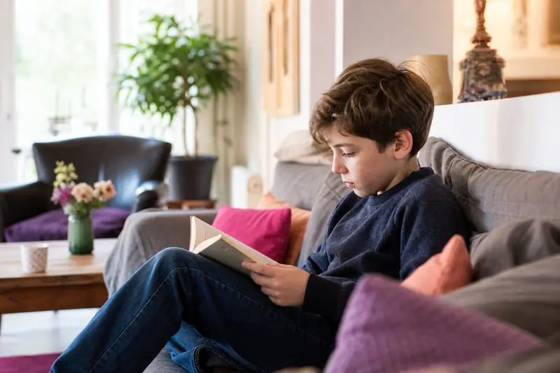 Enfant d'une dizaine d'années lisant seul sur le canapé du salon familial, lumière naturelle douce d'après-midi.