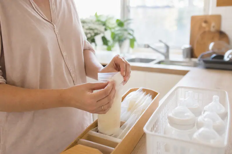 Parent étiquetant un petit sac de conservation de lait maternel avec la date de tirage avant de le placer au congélateur.