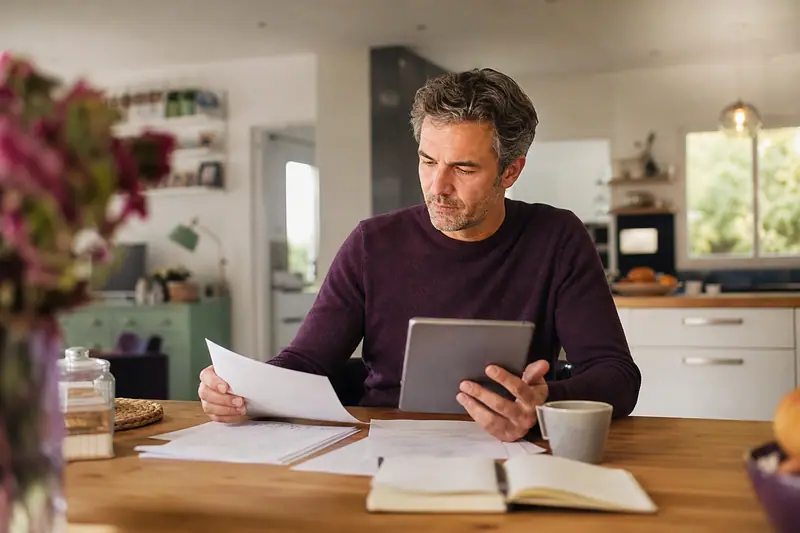 Parent consultant les conditions générales d'un contrat de mutuelle santé sur une tablette à la table de la cuisine.