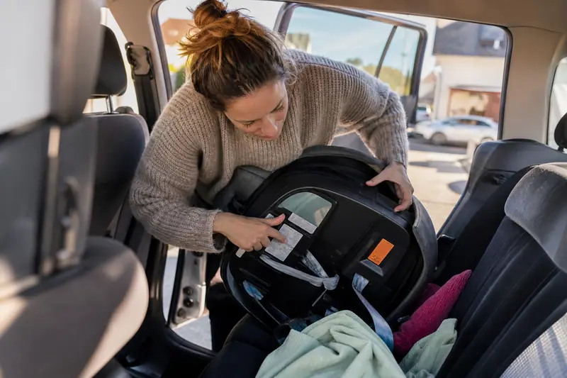 Parent vérifiant l'étiquette au dos d'un siège auto avant de l'installer sur la banquette arrière d'une voiture familiale.
