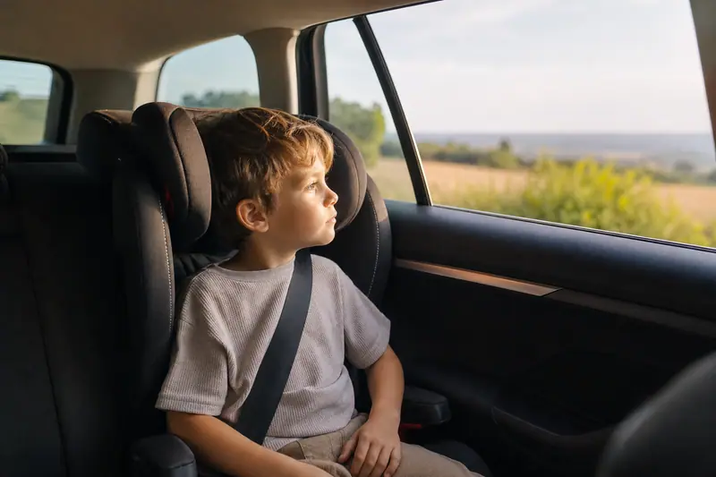 Enfant installé dans un siège auto regardant par la fenêtre d'une voiture en mouvement, lumière naturelle douce.
