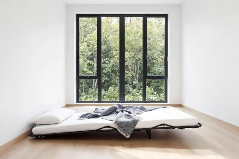 Deux adultes transportent le carton compact d'un matelas roulé compressé dans l'entrée d'un logement familial.