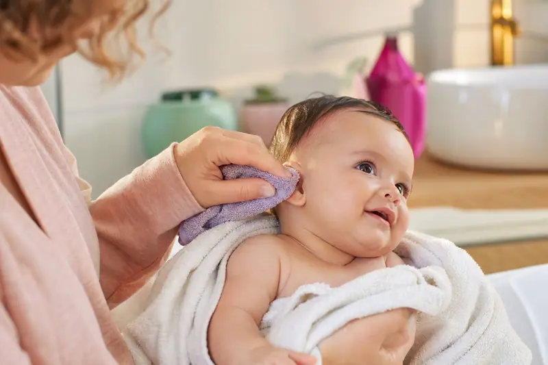 Parent nettoyant délicatement le pavillon de l'oreille d'un bébé avec un gant de toilette doux après le bain.