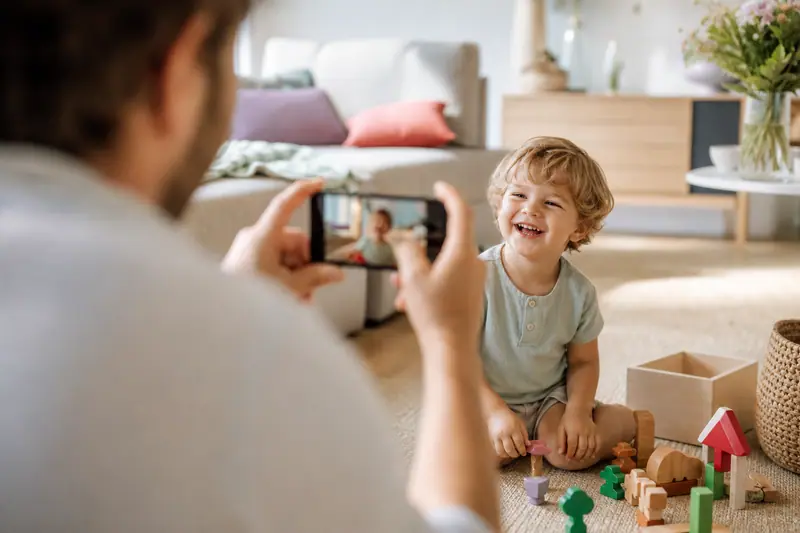 Un parent photographie un enfant qui joue dans un parc avec un smartphone protégé par une coque.