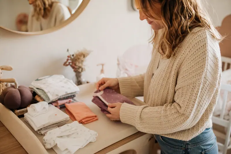 Parent pliant de petits vêtements de naissance de différentes tailles sur une table à langer avant l'arrivée du bébé.